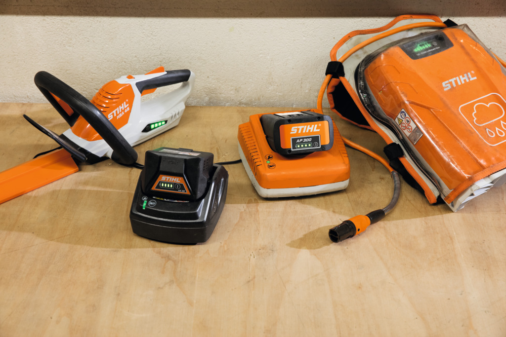 STIHL Hedge trimmer next to various STIHL batteries on a bench