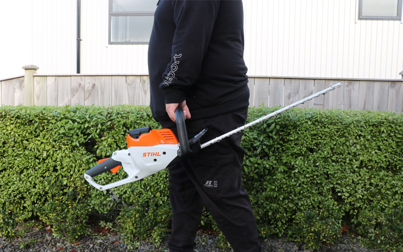 Man holding STIHL HSA 60 Battery Cordless Hedgetrimmer in front of hedge