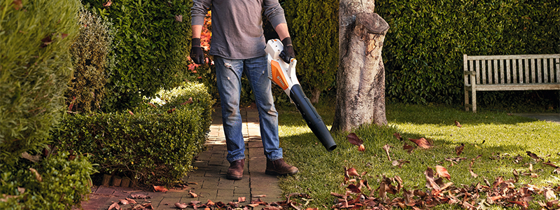 Man blows away autumn leaves on a side path in the garden with STIHL blower