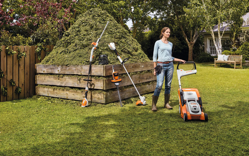 The STIHL AK Battery range in a garden with a lady that has just finished the lawns